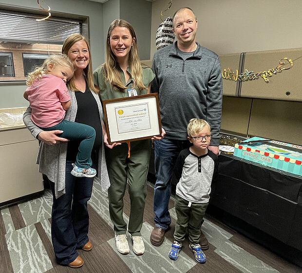 Photo of NDSU Nursing alum Brooke Feltman, DNP, holding a framed certificate, surrounded by patient's family that she helped, including a mother, father and two small children.